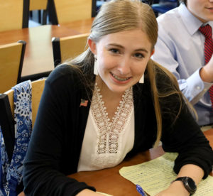 High school student in professional attire smiles while sitting in front of notes