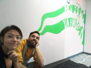 Woman and man crouch next to an indoor mural in progress