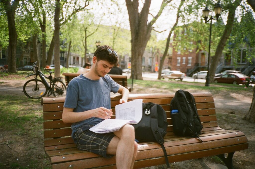 A young man looks down at sheet music on a park bench